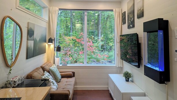 Een moderne kamer met een groot raam, een bank, een televisie en een klein tafeltje.
