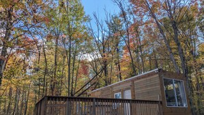 Een houten chalet met terras, omgeven door herfstbomen.