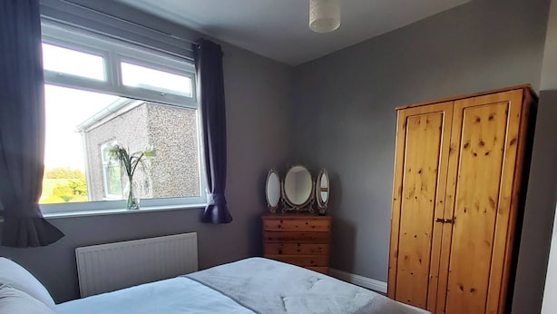A bedroom with a double bed, a wooden wardrobe, a dresser with mirrors, and a window with curtains. - Room-peaceful Village Retreat (Morpeth)