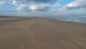 A wide sandy beach with gentle waves and a partly cloudy sky. - Room-peaceful Village Retreat (Morpeth)