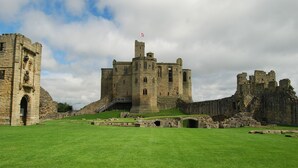 A historic castle with a central tower, a moat, and ruins on the right. - Room-peaceful Village Retreat (Morpeth)
