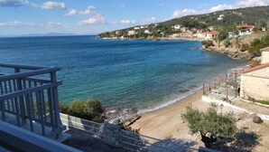 A coastal view with a beach, a rocky shoreline, and buildings on a hillside. - Nicolas (South Pelion)