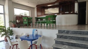 A hotel lobby with a blue table, white chairs, a green bench, a wooden reception desk, and a staircase. - Nicolas (South Pelion)