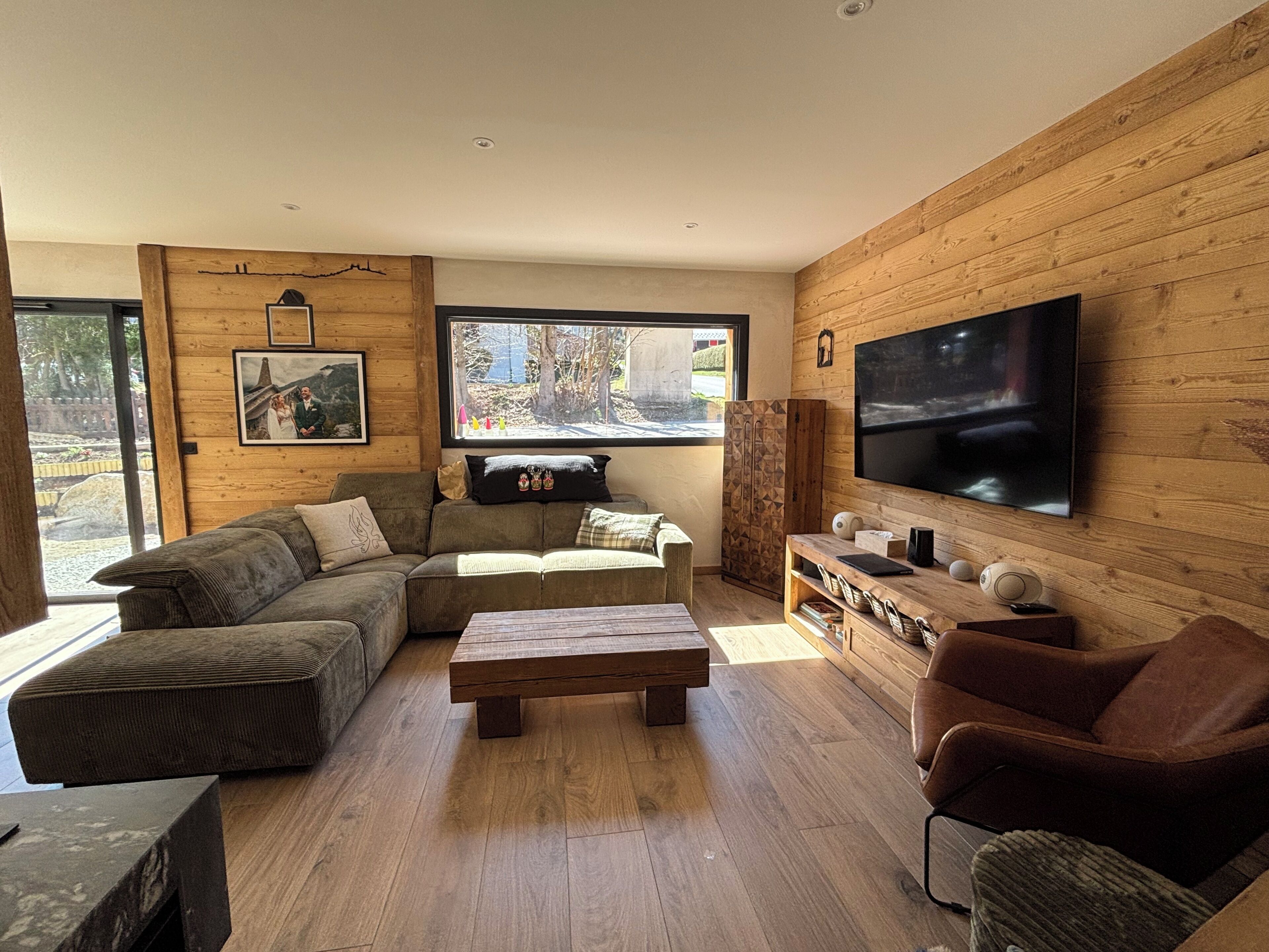 Un salon moderne avec un canapé d’angle, une table basse, un téléviseur et un mur en bois.