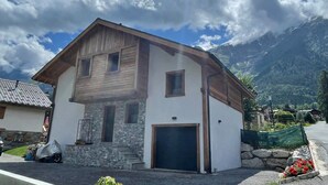 En toetages bygning med en stenfacade, garage og et bjerg i baggrunden.