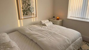 A bedroom with a bed, a nightstand, a lit candle, a window, and a framed botanical illustration. - Near Etihad/coop Live - Parking - Wifi - Sleeps 4 (Manchester)