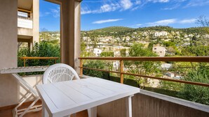 A balcony with a white table and chair, a view of a town, and a railing. - Air-conditioned flat for 4 people, with a swimming pool and balcony (Grasse)