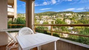 A balcony with a white table and chair, a view of a town, and a railing. - Air-conditioned flat for 4 people, with a swimming pool and balcony (Grasse)
