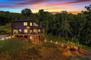 A two-story house with a deck, surrounded by trees and a sunset sky. - Hot Tub Cabin| Pizza Oven | 3 King Suites | Winery (Talking Rock)