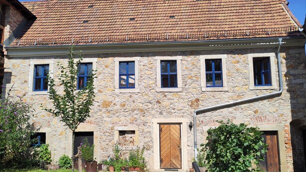 Un edificio in pietra con tetto in tegole, diverse finestre e un portone.