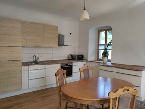 Eine moderne Küche mit Holzausstattung, einem Esstisch, Stühlen, einer Mikrowelle und einem Fenster mit einer Pflanze.