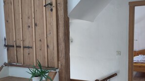 Una scala in legno con corrimano, una pianta in vaso e un letto nella stanza adiacente.
