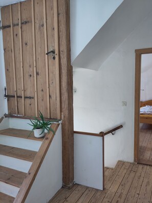 Eine Holztreppe mit Handlauf, ein Blumentopf und ein Bett im angrenzenden Zimmer.