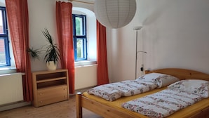 Una camera da letto con un letto di legno, un termosifone, una pianta in vaso e una finestra con tende.
