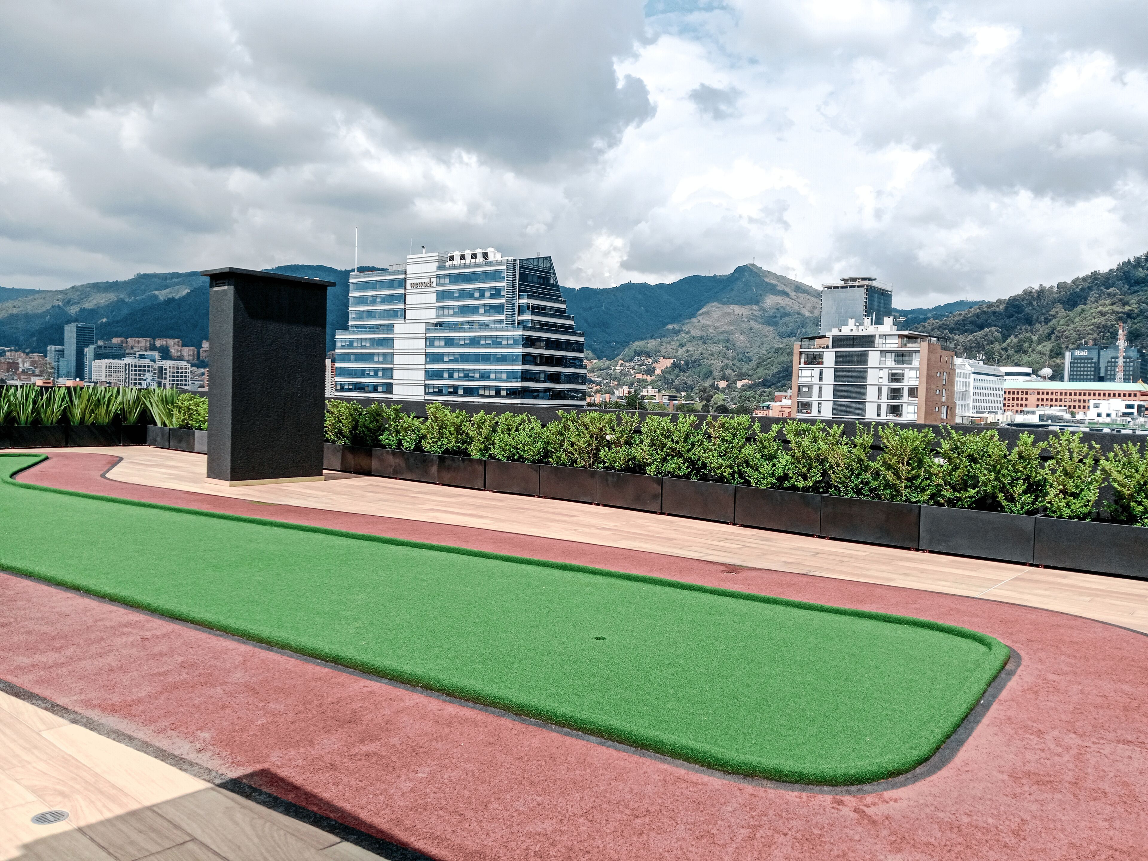 A rooftop with artificial grass, a red running track, and a black structure.