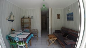 A compact living space with a dining table, chairs, a sofa, a small table, and a hanging light fixture. - Sea, Relaxation and Pink Granite / 3-person apartment 300m from the beach (Trébeurden)