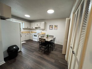 A compact kitchen with white cabinets, a stove, and a dining table with chairs.