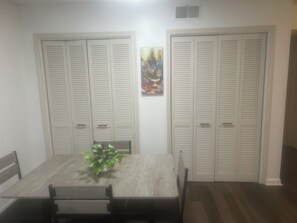 A dining area with a wooden table and chairs, flanked by two white louvered closets, and a small potted plant on the table.