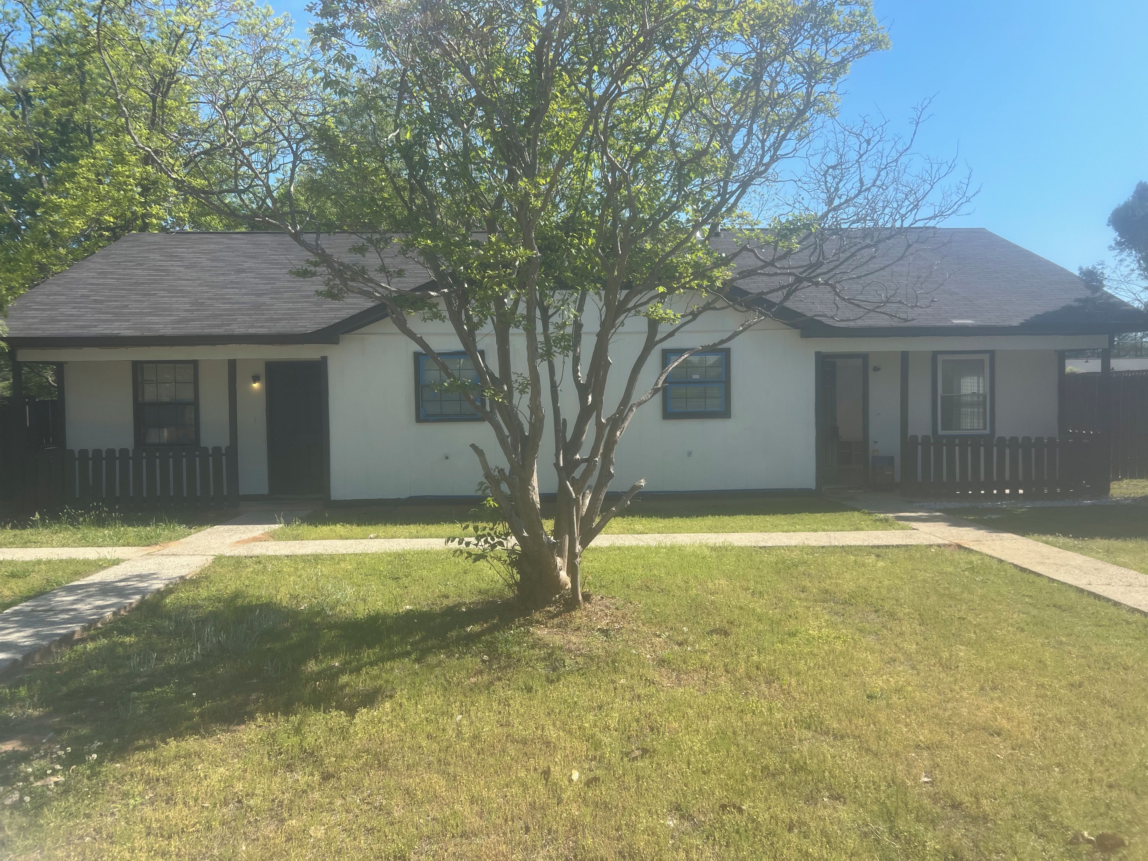 A single-story house with a front porch, a small tree, and a clear sky.