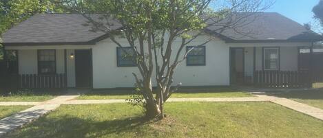A single-story house with a front porch, a small tree, and a clear sky.