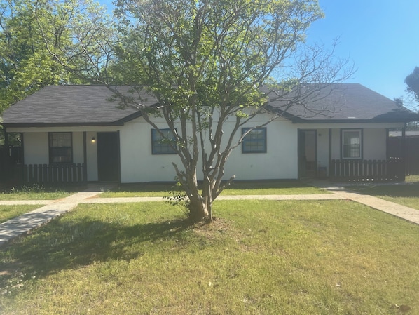 A single-story house with a front porch, a small tree, and a clear sky.