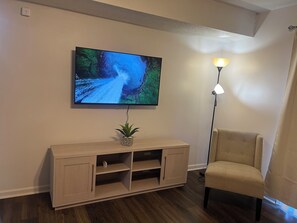 A room with a television mounted on the wall, a wooden cabinet below it, a floor lamp, and a chair.