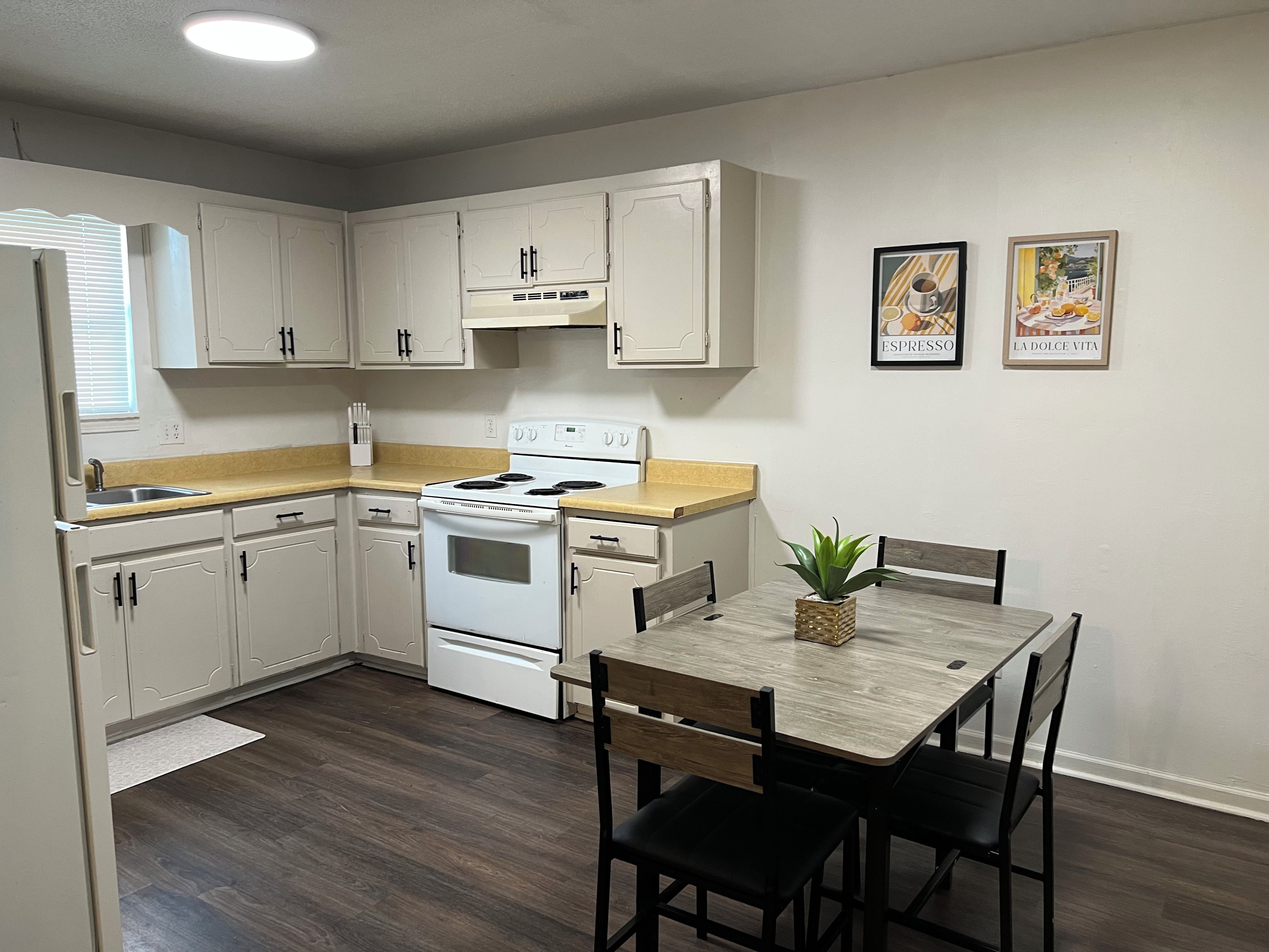 A compact kitchen with white cabinets, a stove, and a dining table with chairs.