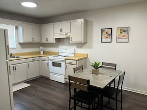 A compact kitchen with white cabinets, a stove, and a dining table with chairs.