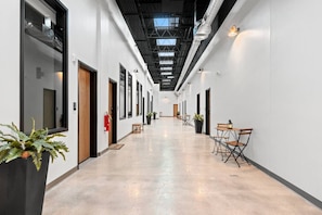 A long corridor with doors on both sides, potted plants, and a fire extinguisher.