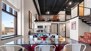 A modern interior with a glass dining table, white chairs, a red and white patterned sofa, and a kitchen area with stainless steel appliances.