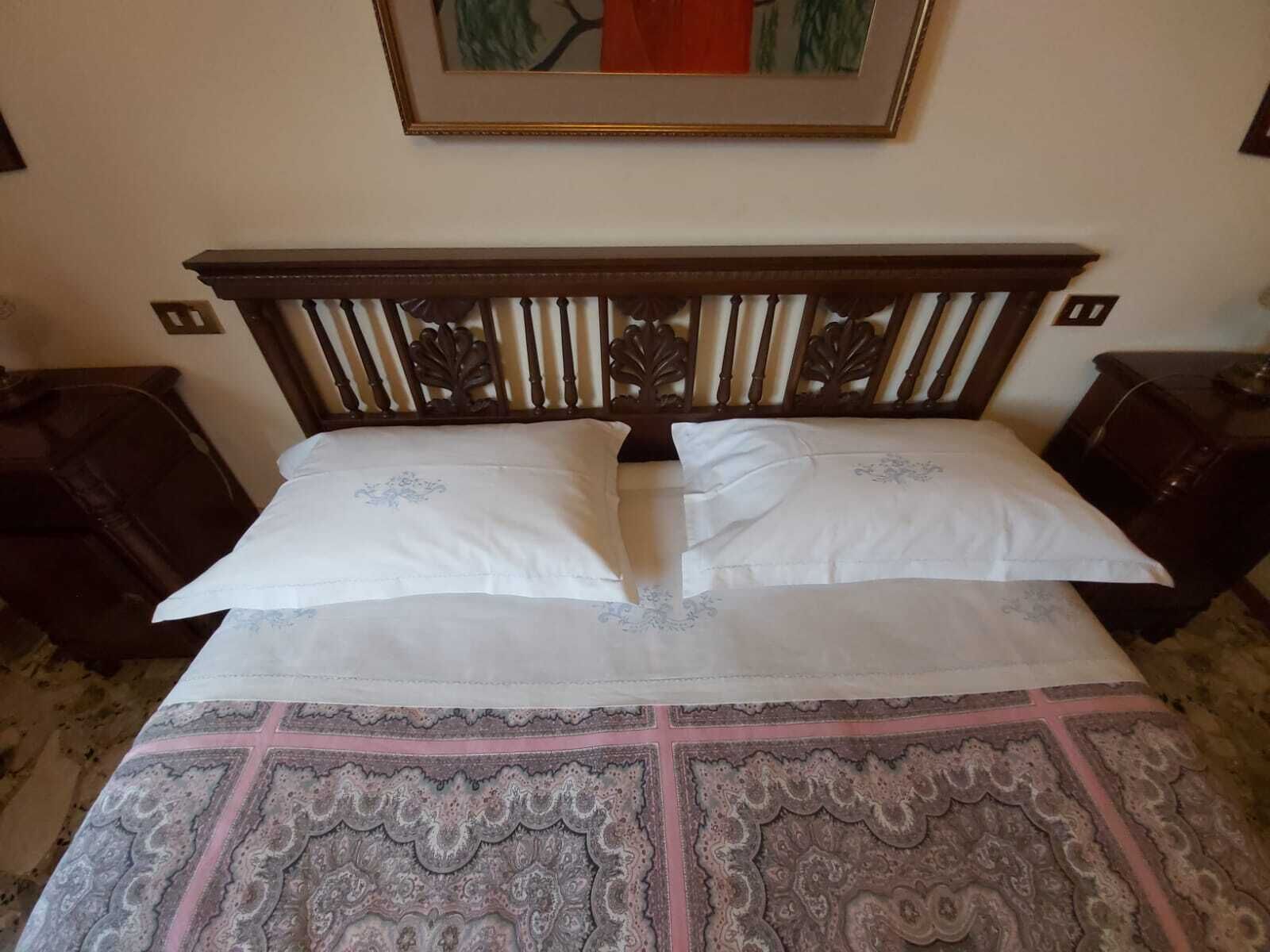 A bed with a wooden headboard, two pillows, and a patterned bedspread.
