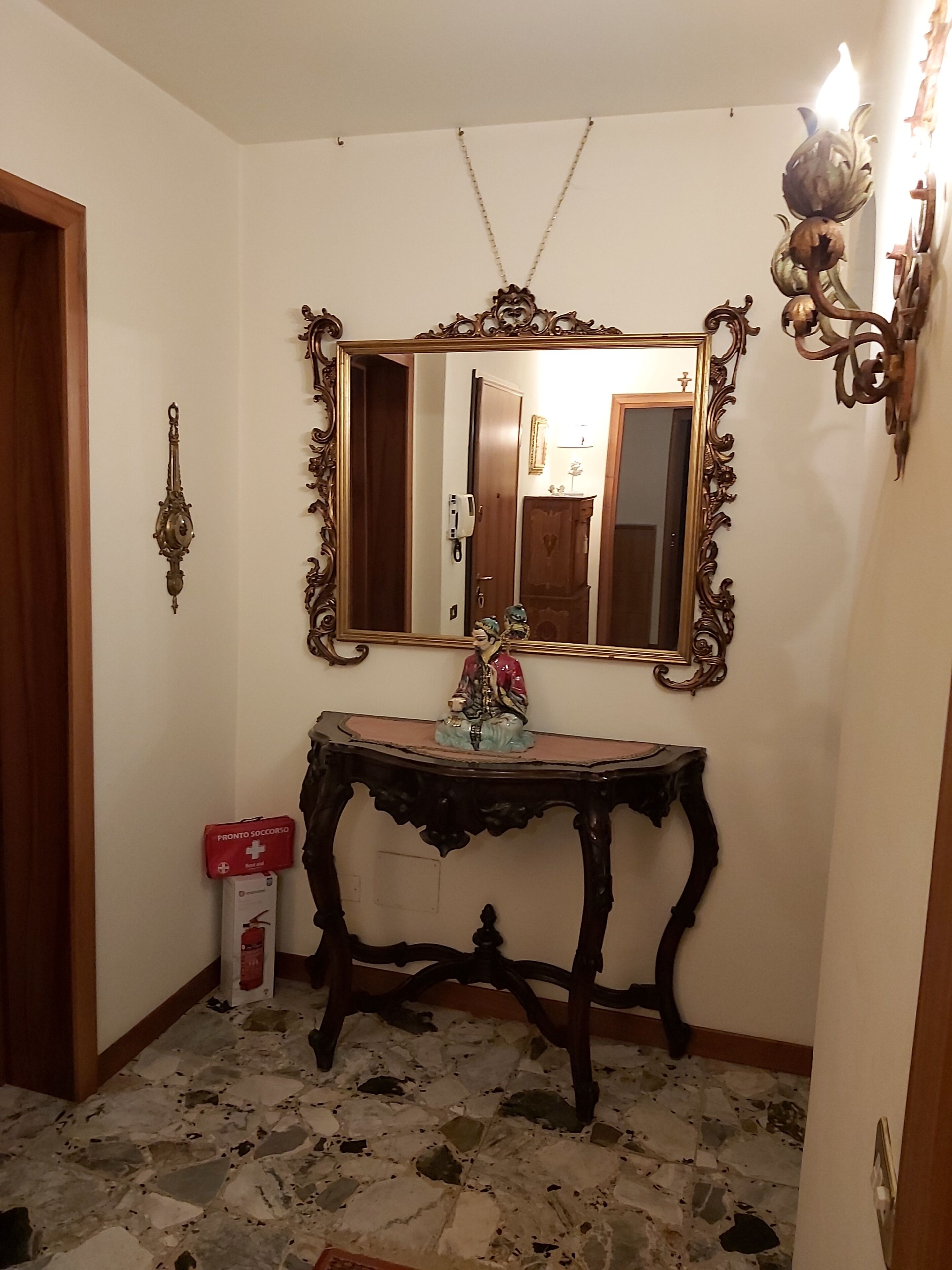 Une pièce avec un miroir, une statue, une porte en bois et un sol carrelé.
