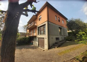 Un edificio de dos pisos con un balcón en el nivel superior, una puerta de garaje y un camino de entrada pavimentado.