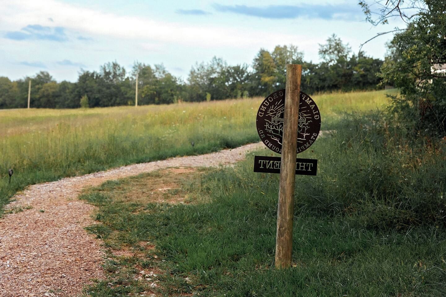 Een landweg die leidt naar een bord met een rond embleem en een rechthoekig bord.