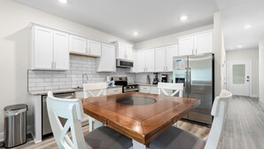 Une cuisine moderne avec des meubles blancs, un réfrigérateur en acier inoxydable et une table à manger en bois.