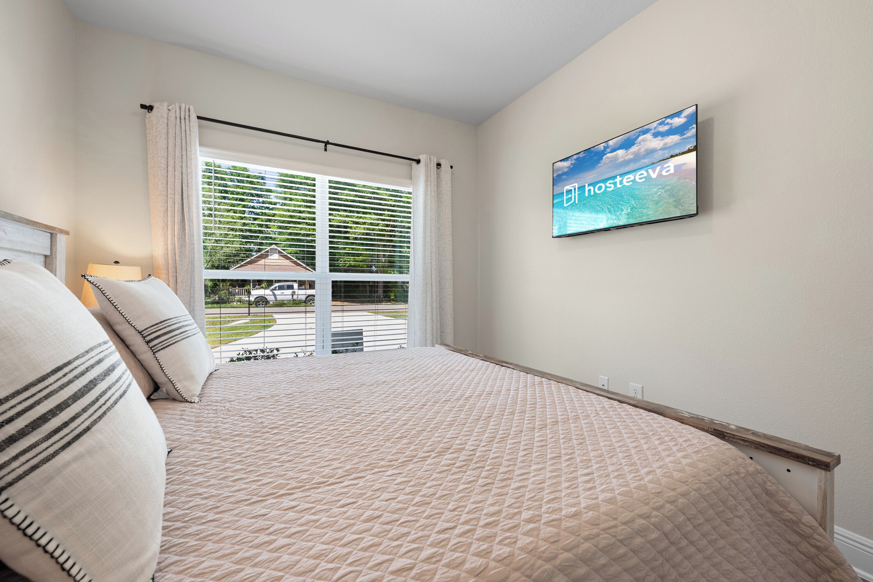 Un dormitorio con cama, televisor montado en la pared y vistas al exterior a través de una ventana.