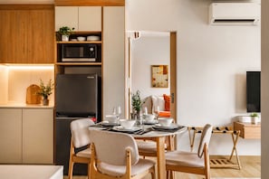 A modern kitchen with a refrigerator, microwave, and dining area with chairs and a table set for two. - Luxury 2BR in Laguna•Golf View•Skypark Pool (Choeng Thale)