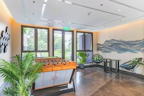 A modern indoor space with a foosball table, seating area, and a large window providing a view of greenery. - Luxury 2br in Laguna - Golf view - skypark pool (Choeng Thale)