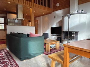 A cozy living room with a sofa, a TV, a fireplace, and a wooden ceiling.
