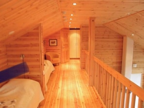A narrow wooden hallway with a bed on the left and a staircase on the right.