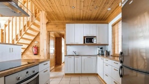 A modern kitchen with wooden beams, white cabinets, stainless steel appliances, and a visible fire extinguisher. - Charming Lapland Villa With Mountain Views, Private Sauna and Outdoor Hottub (Pelkosenniemi)