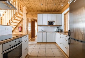 A modern kitchen with wooden beams, white cabinets, stainless steel appliances, and a visible fire extinguisher. - Charming Lapland Villa With Mountain Views and Private Sauna (Pelkosenniemi)
