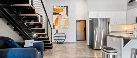 A modern kitchen with stainless steel appliances, a dining area with a blue sofa, and a staircase with black railings.