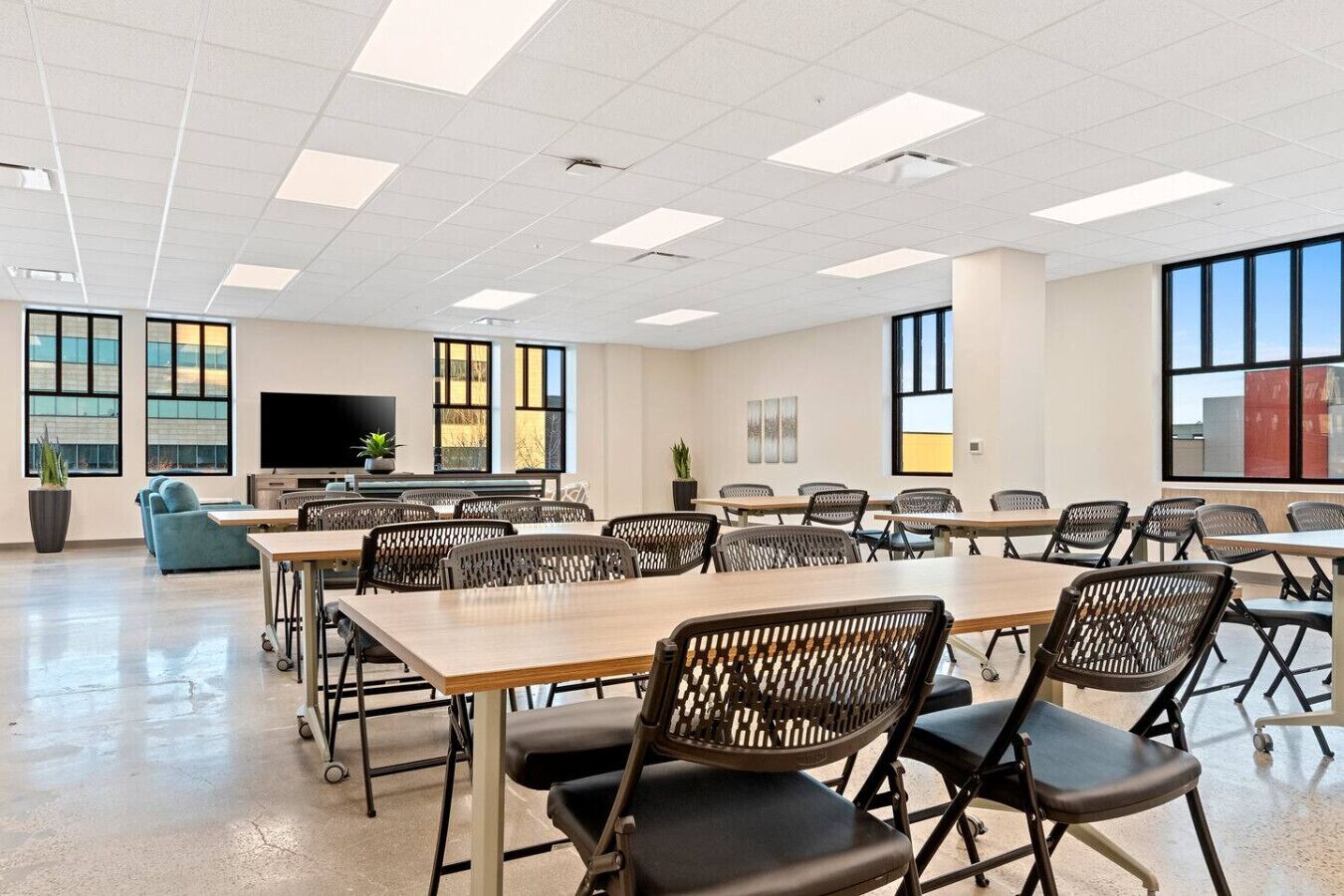 A conference room with tables and chairs, large windows, a flat-screen TV, and a plant.