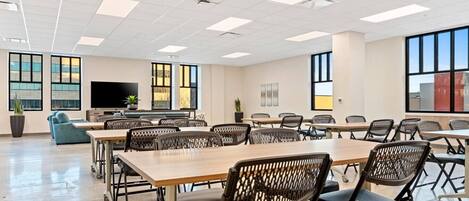 A conference room with tables and chairs, large windows, a flat-screen TV, and a plant.
