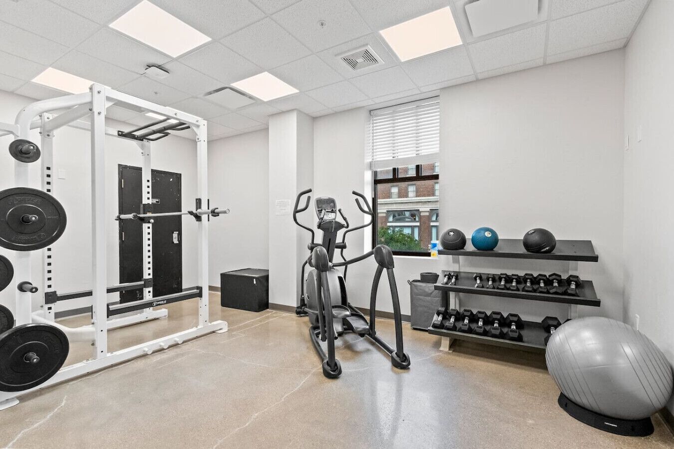 Un gimnasio con una banca de pesas, mancuernas, cinta de correr y pelotas de ejercicio.