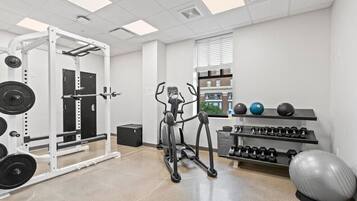 Un gimnasio con una banca de pesas, mancuernas, cinta de correr y pelotas de ejercicio.