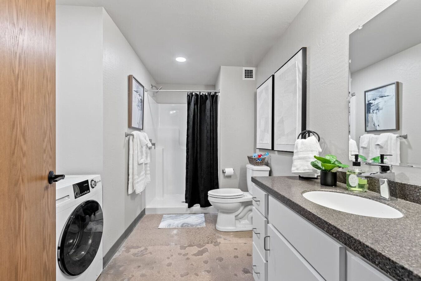 A modern bathroom with a washing machine, toilet, shower, and a sink with a mirror.
