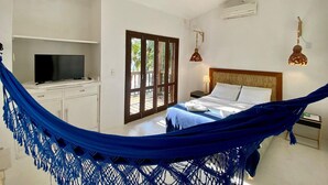 A bedroom with a bed, a TV, a desk, a hammock, and a view of the outdoors. - Casa Janaina (Ilhabela)