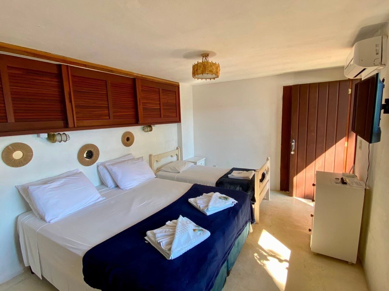A hotel room with two beds, a small desk, a refrigerator, and a wardrobe.